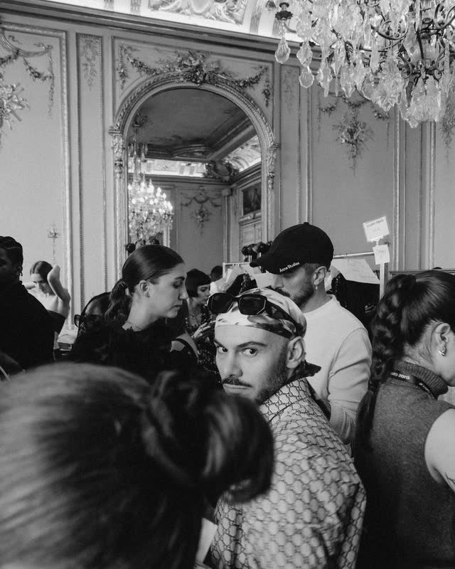 Hairstylists at work in a crowded, gilded backstage room