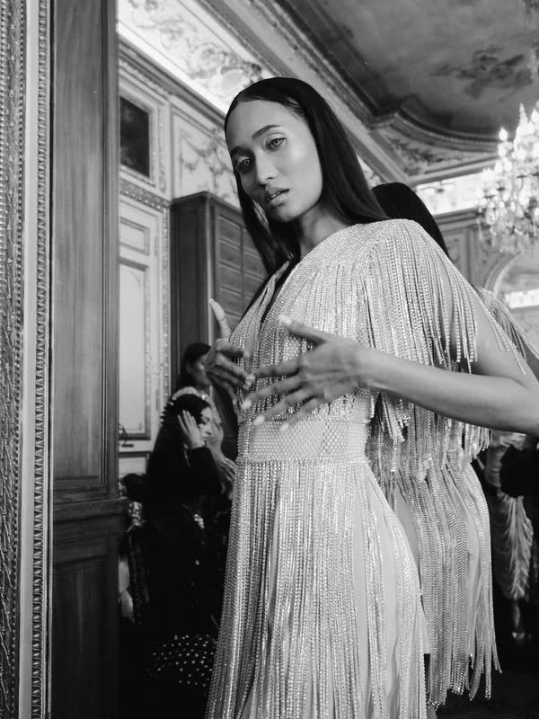 Model adjusting a fringed dress in a mirrored salon