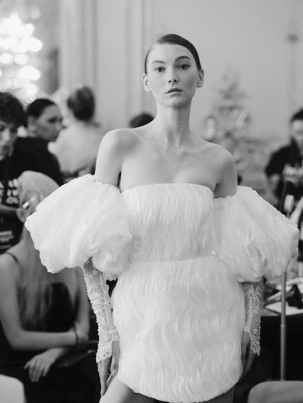 Model on the runway in a white off-shoulder feathered dress